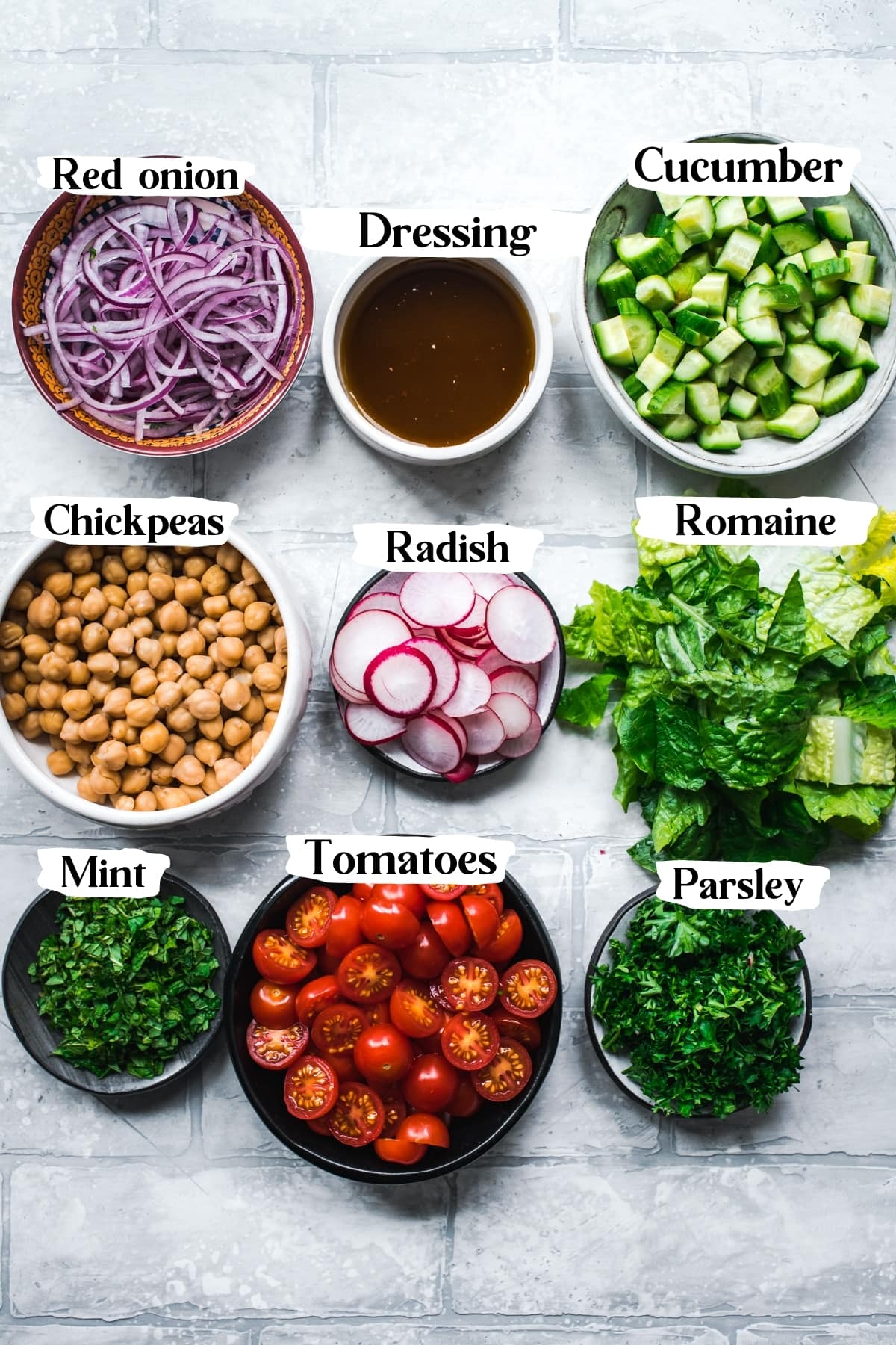 overhead view of ingredients for chickpea fattoush salad in small bowls on tile backdrop. 