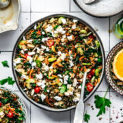 overhead view of vegan french lentil salad in a large bowl with serving spoon on white tile background.