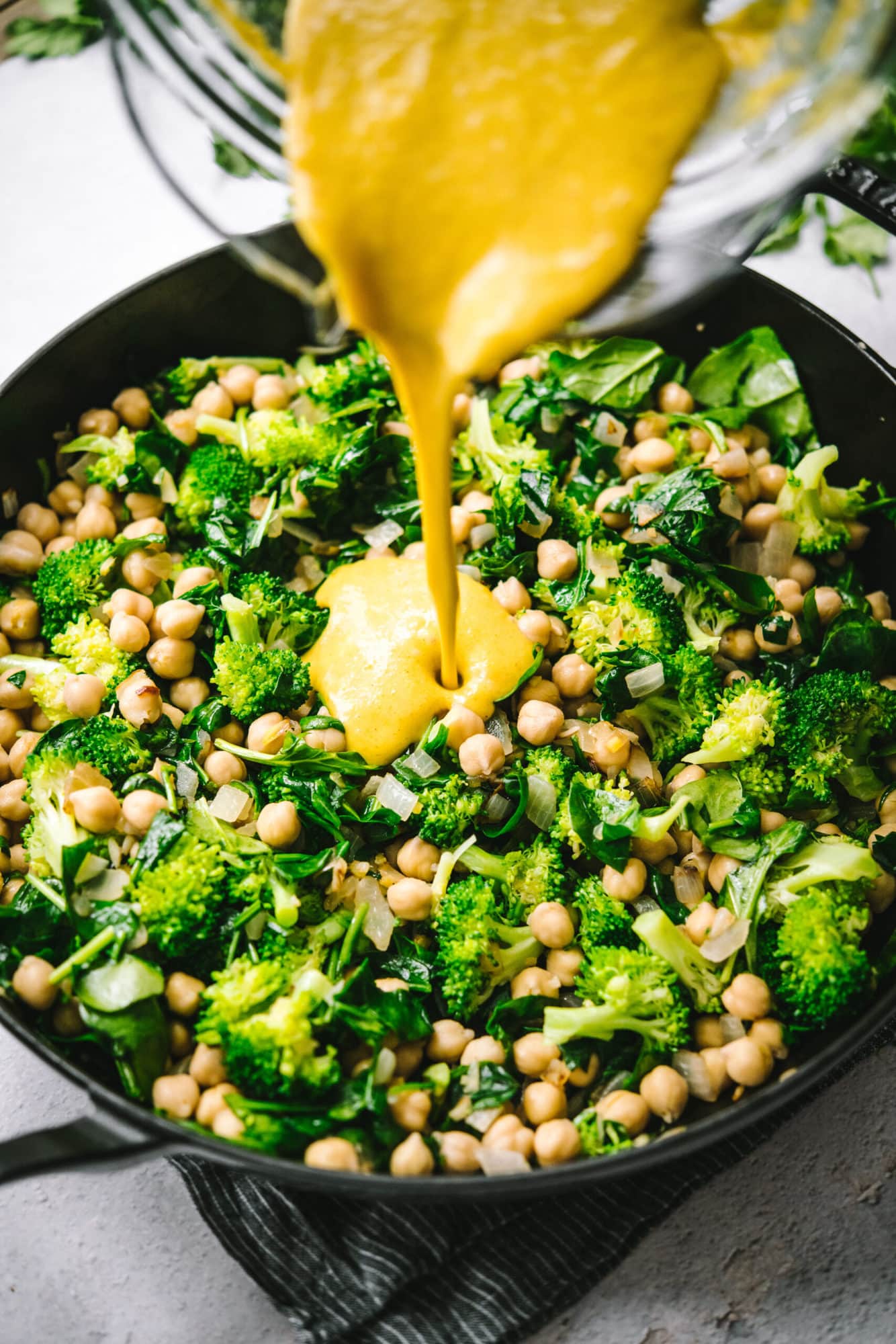 pouring mango curry sauce into chickpea curry in large skillet.