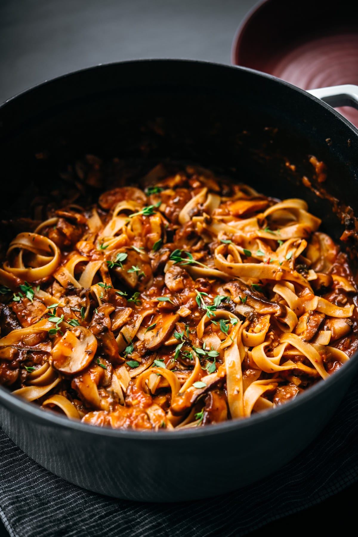 close up view of vegan mushroom ragu over pasta in a large white dutch oven. 