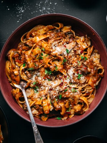 overhead view of vegan mushroom ragu over pasta in a red bowl.