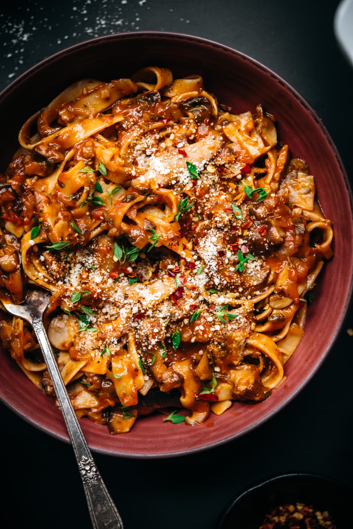 overhead view of vegan mushroom ragu over pasta in a red bowl. 