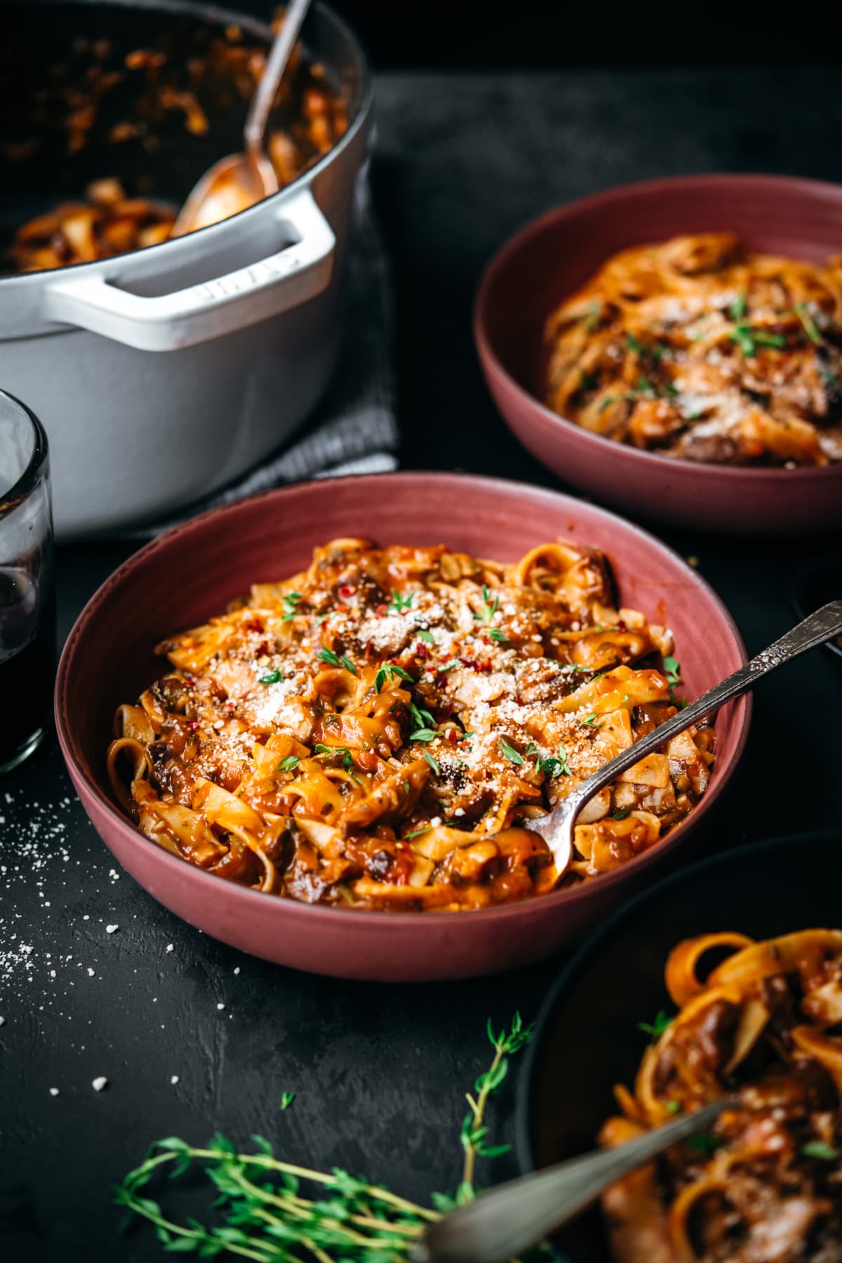 side view of vegan mushroom ragu over pasta in a red bowl.