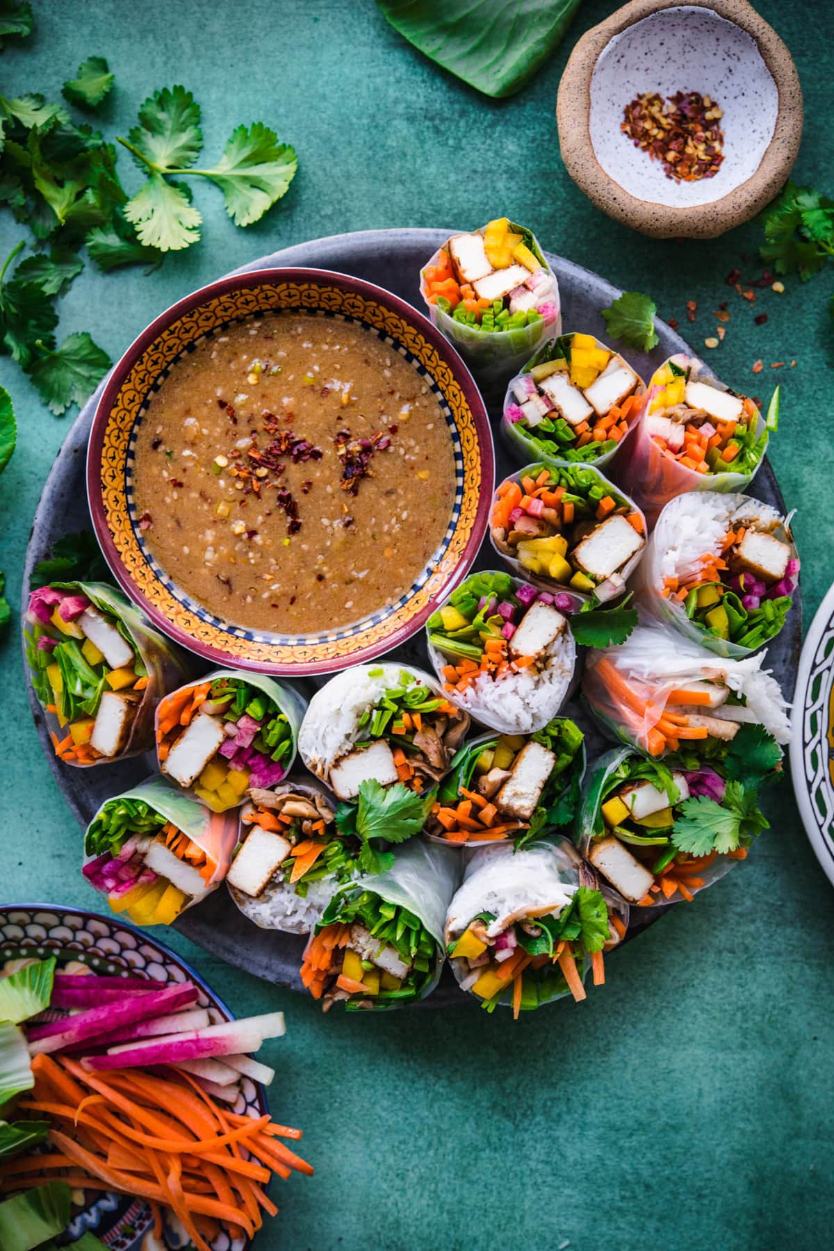 overhead view of tofu vegetable summer rolls on a circular platter with bowl of miso dipping sauce. 