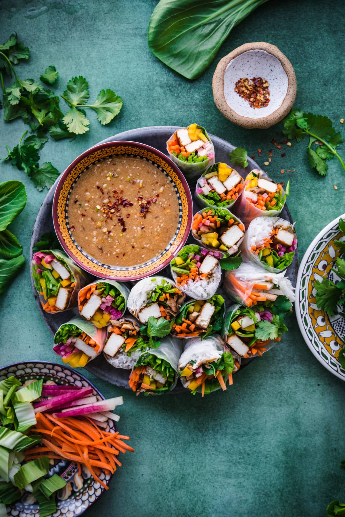 overhead view of tofu vegetable summer rolls on a circular platter with bowl of miso dipping sauce. 