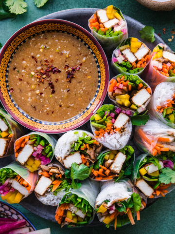 overhead view of tofu vegetable summer rolls on a circular platter with bowl of miso dipping sauce.