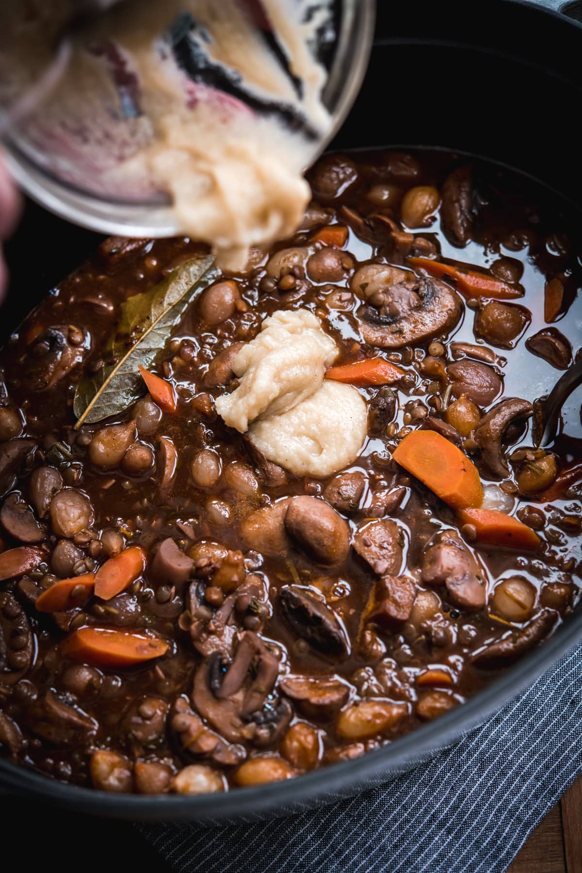 pouring roux into vegan coq au vin in a large pot.