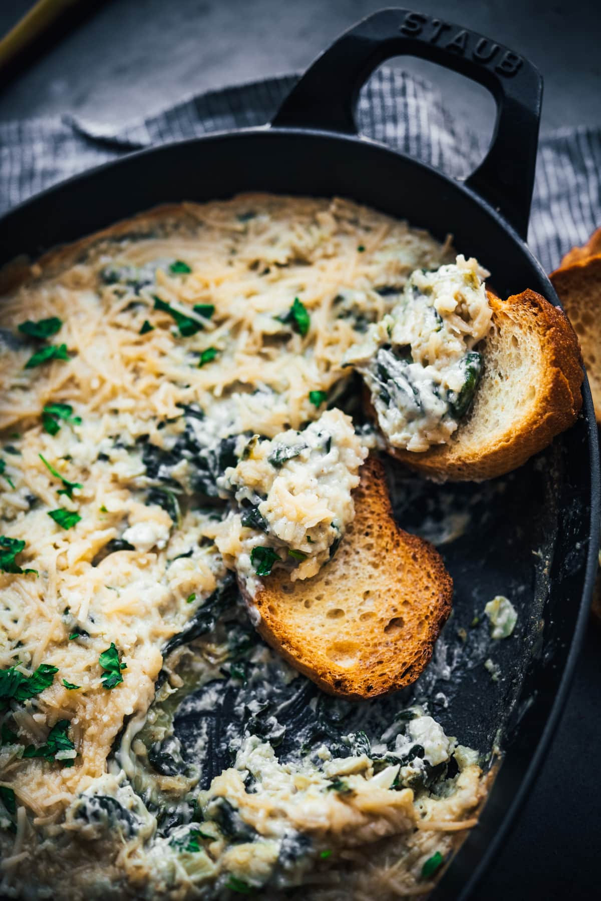close up view of vegan spinach artichoke dip in a skillet with two pieces of toasted baguette for dipping. 