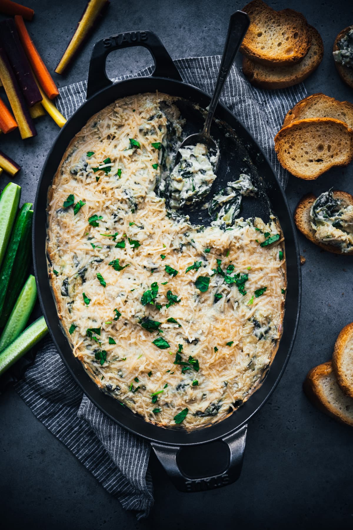 overhead view of vegan spinach artichoke dip in a skillet with toasted bread and veggies for serving. 