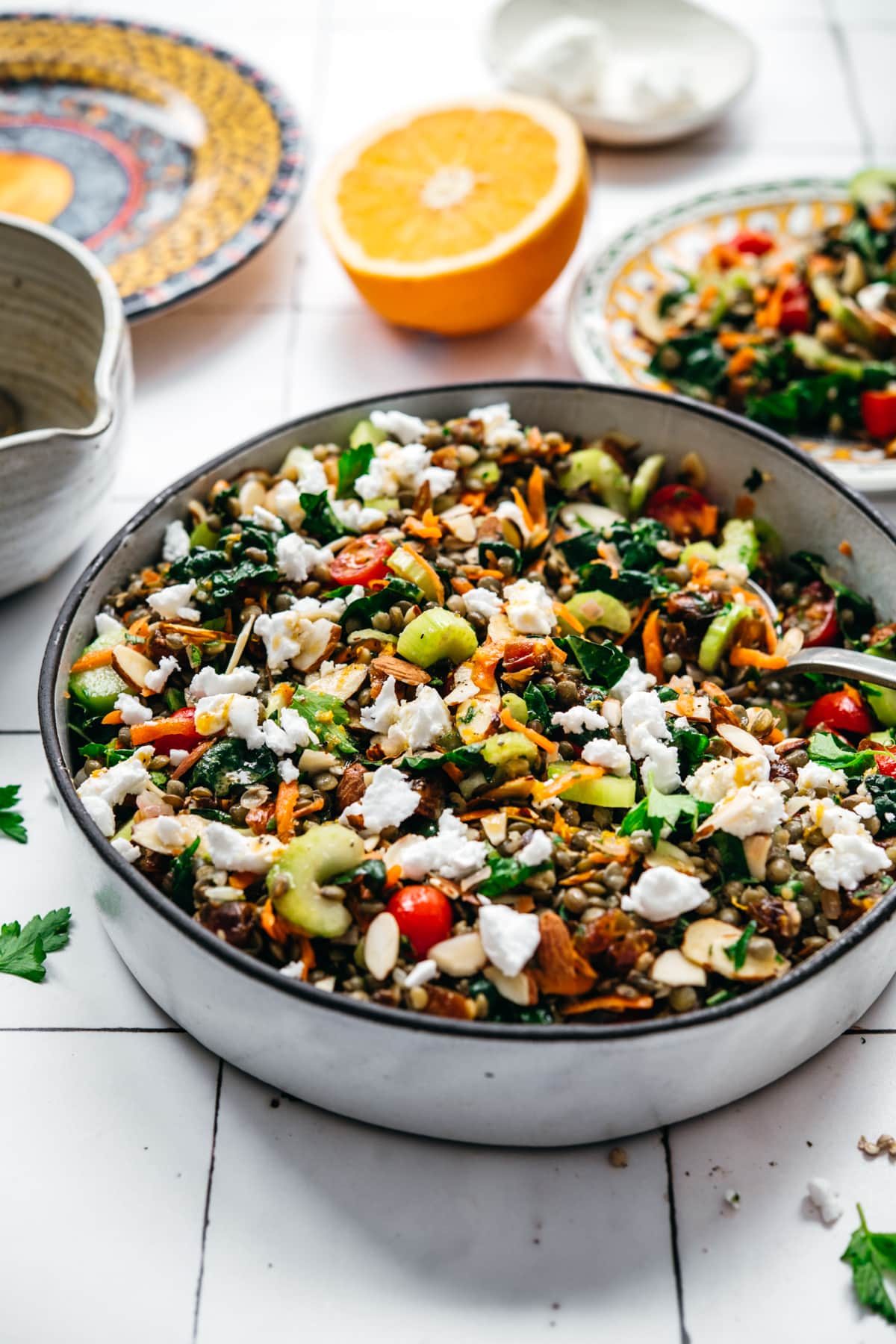 side view of vegan french lentil salad in a large bowl with serving spoon on white tile background.