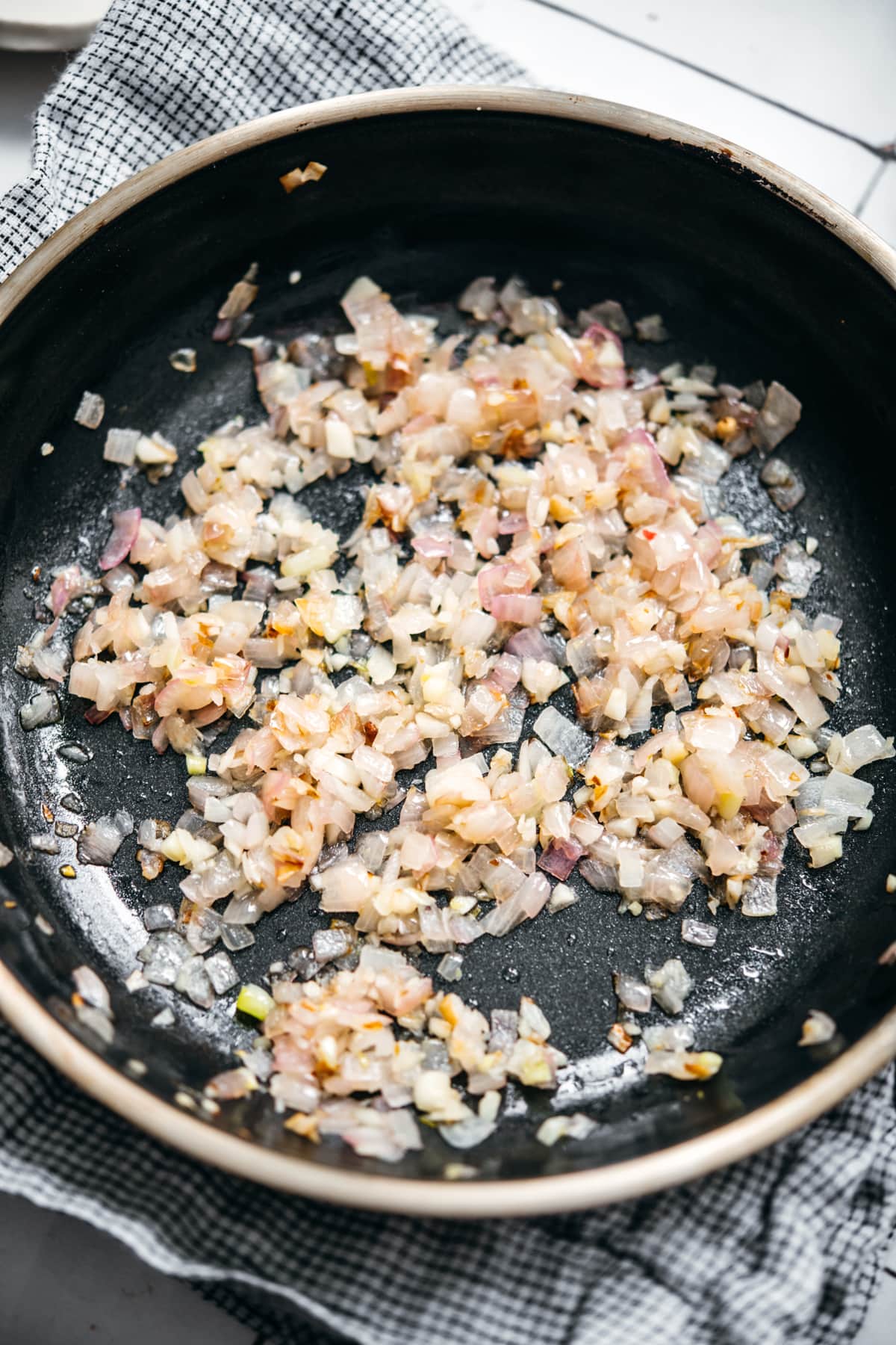 close up view of sautéed shallots and garlic in a pan.