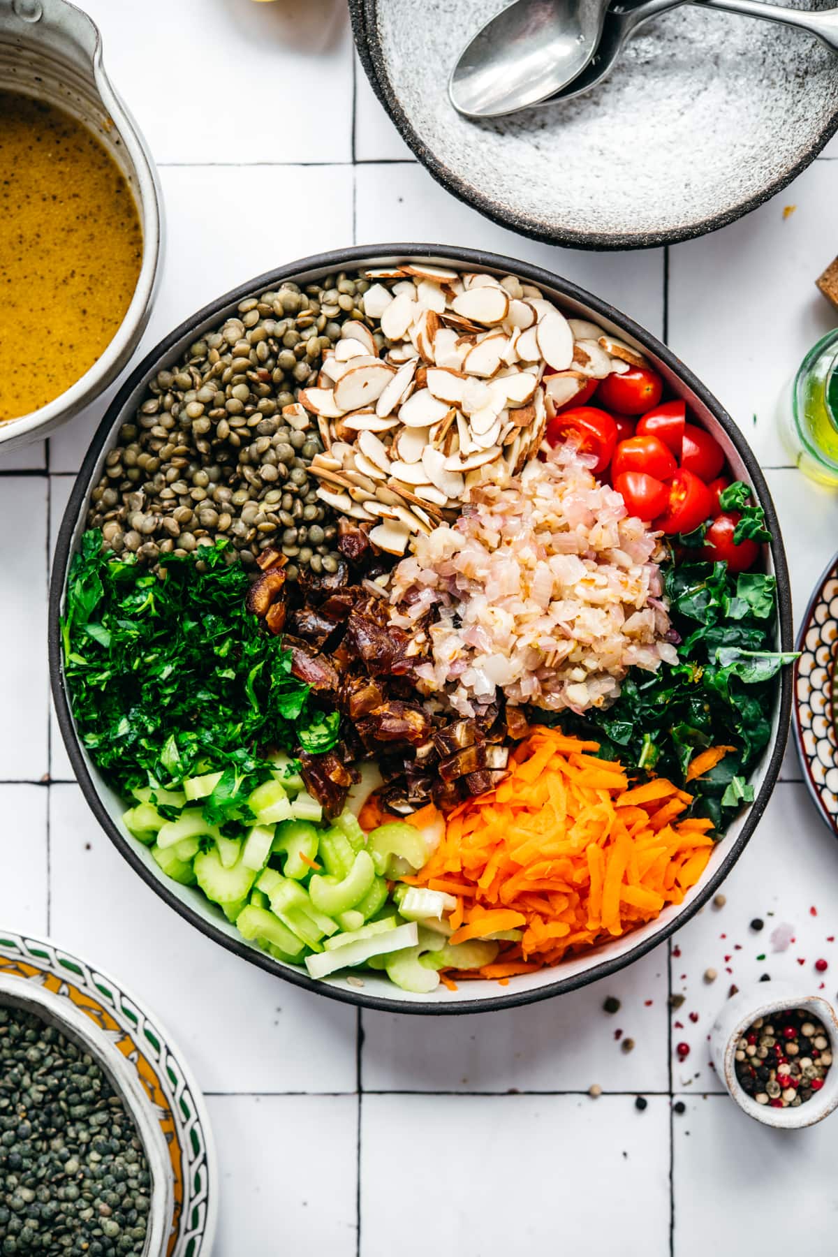 overhead view of vegan french lentil salad in a large bowl with serving spoon on white tile background.