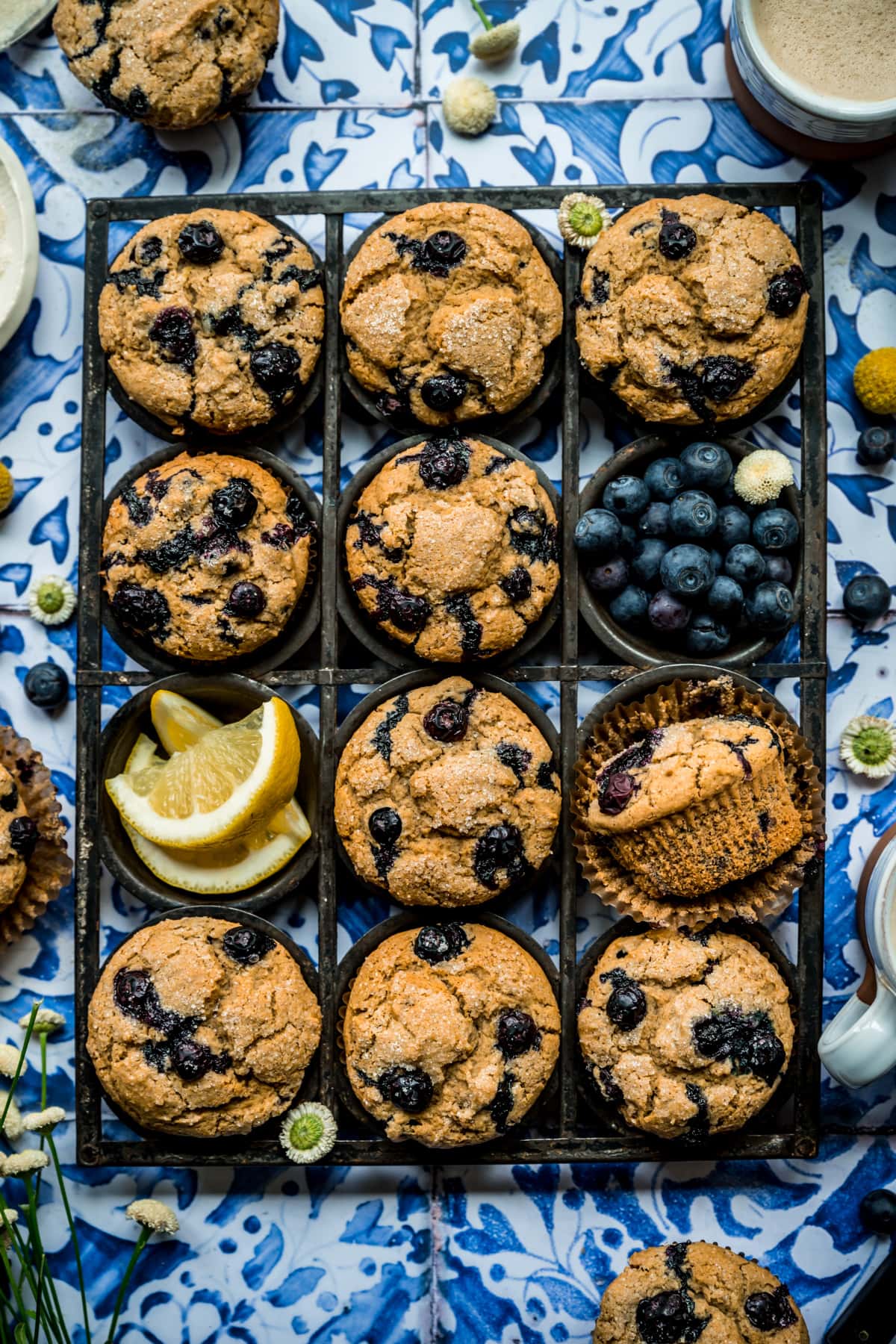 overhead view of vegan blueberry muffins in antique muffin tin on blue tile backdrop.