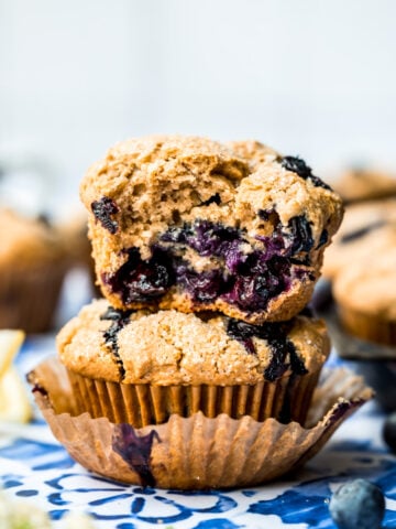 close up side view of two stacked vegan blueberry muffins with the top one cut in half.