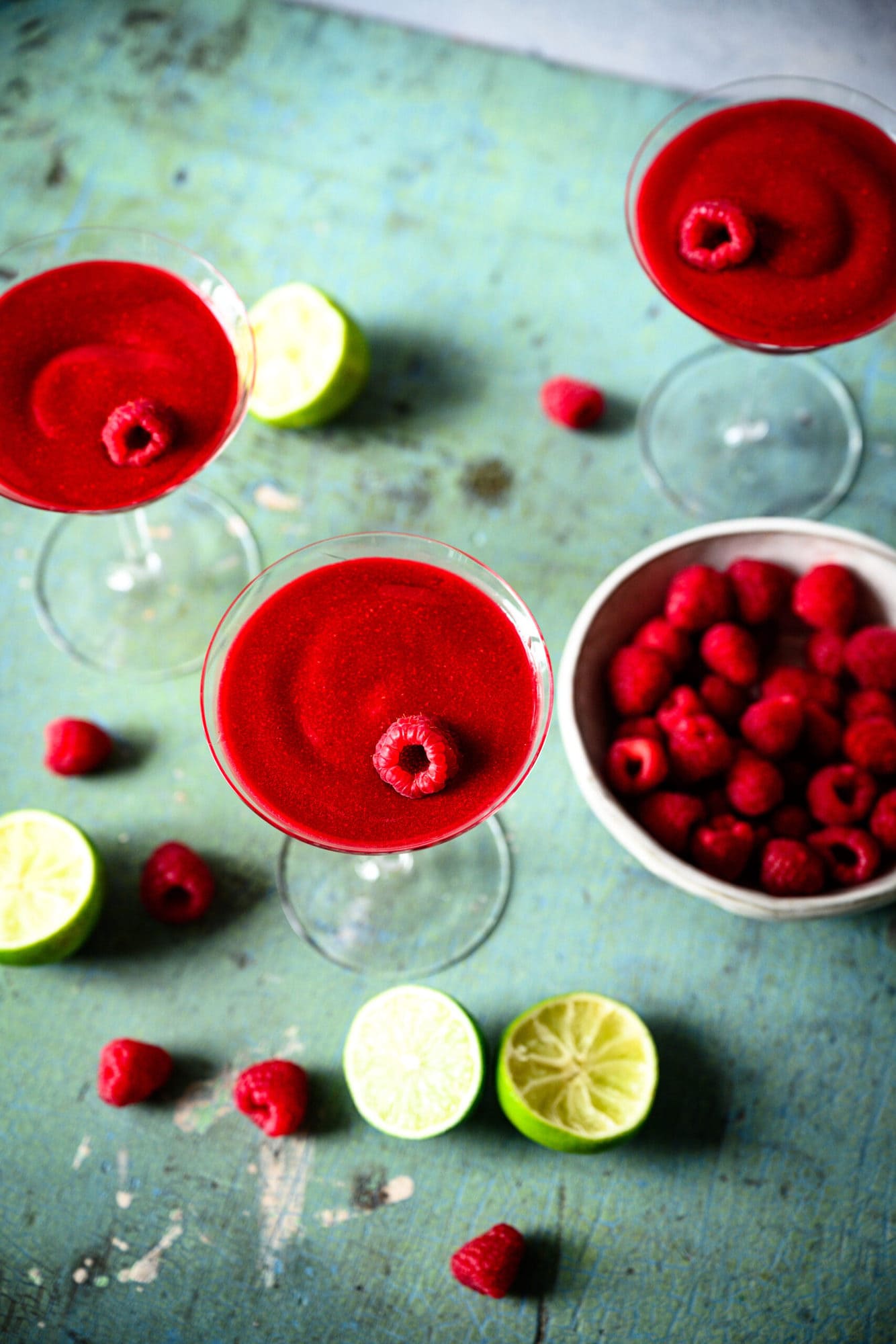 overhead view of frozen raspberry daiquiri in coupe glass with fresh raspberries and lime slices. 