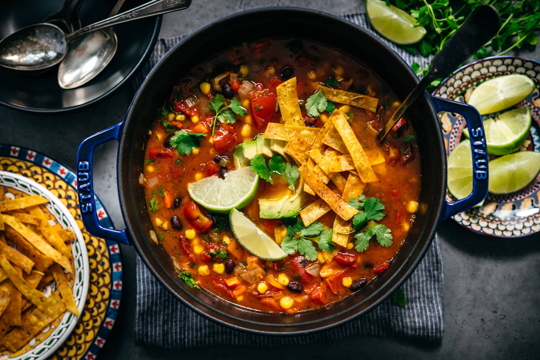 overhead view of vegan tortilla soup in large Staub pot topped with tortilla strips, avocado and cilantro. 