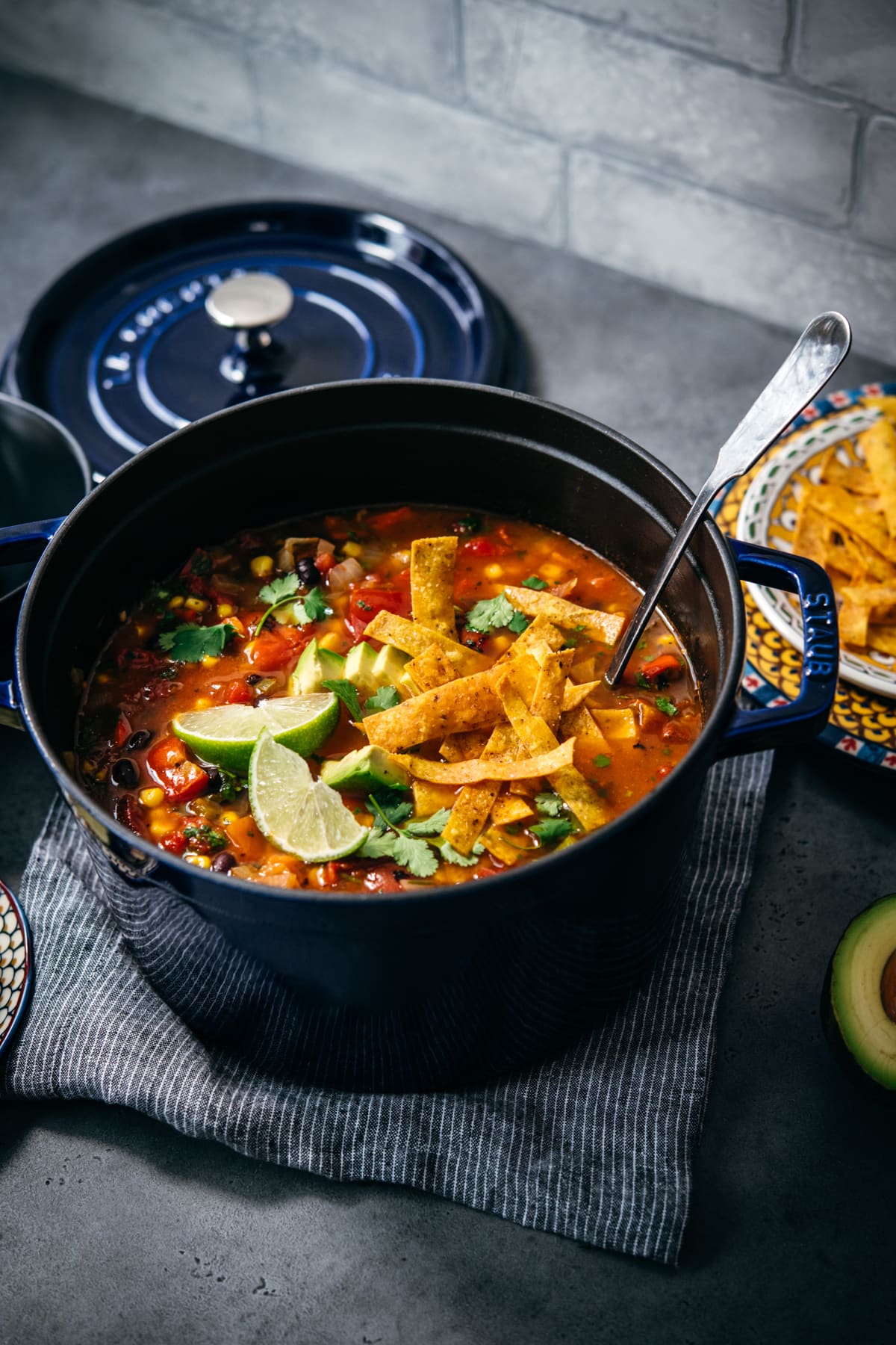 overhead view of vegan tortilla soup in large Staub pot topped with tortilla strips, avocado and cilantro. 