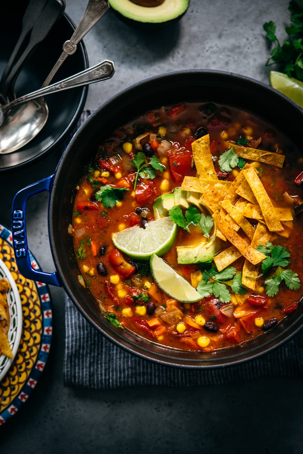 overhead view of vegan tortilla soup in large Staub pot topped with tortilla strips, avocado and cilantro.