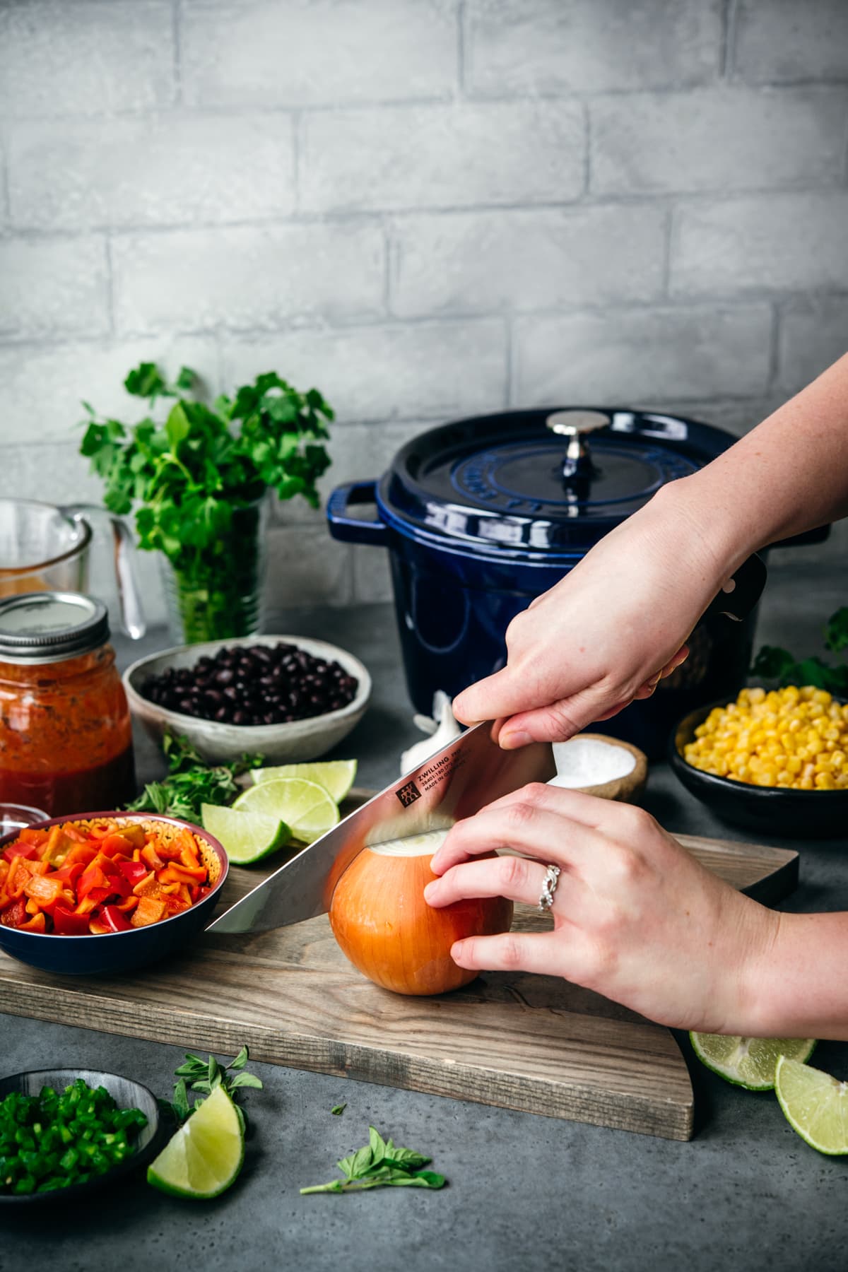 ingredients for tortilla soup on cutting board with person slicing through a yellow onion. 