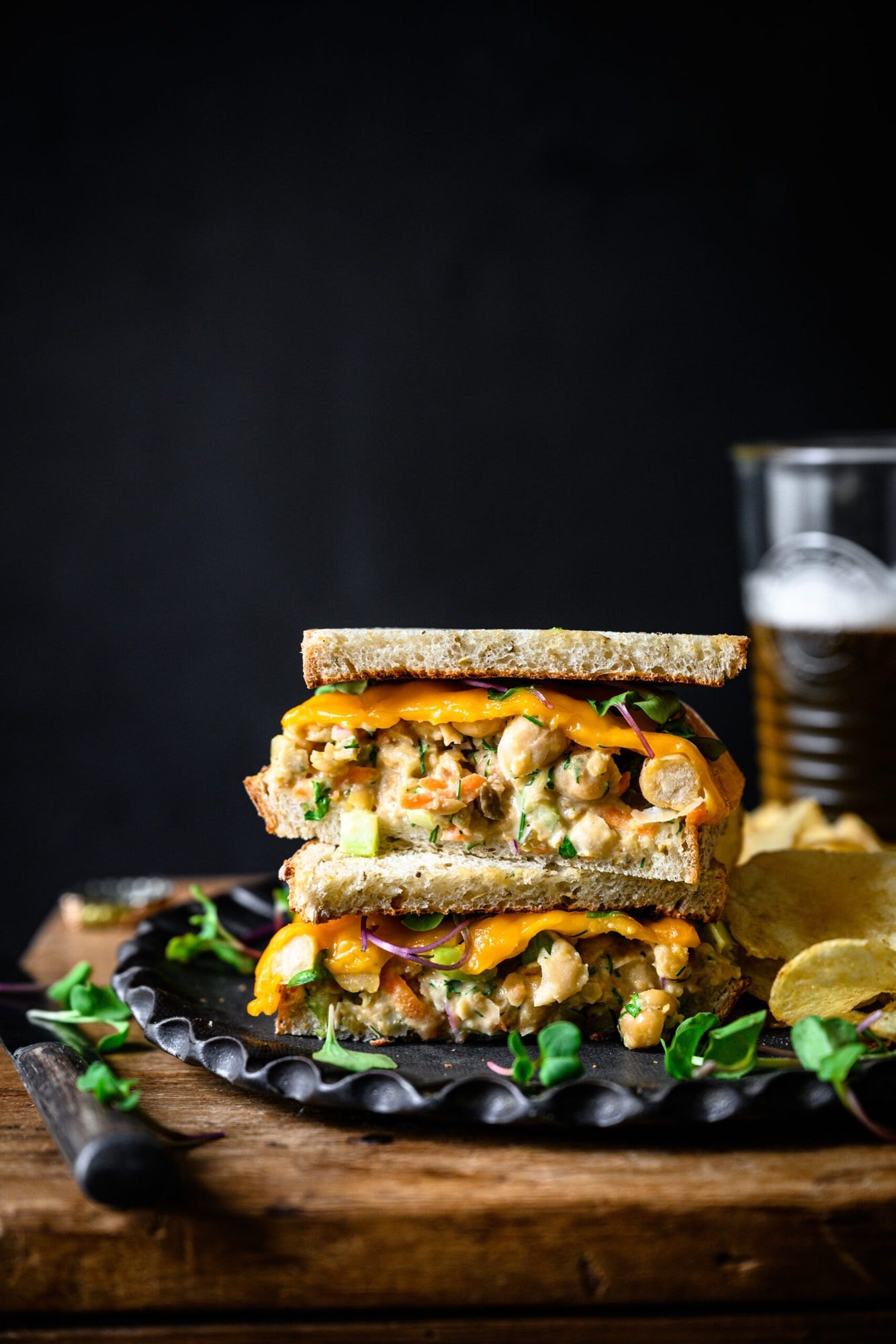 side view of a vegan tuna salad sandwich sliced in half and stacked on a plate with potato chips. 