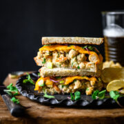 side view of a vegan tuna salad sandwich sliced in half and stacked on a plate with potato chips.