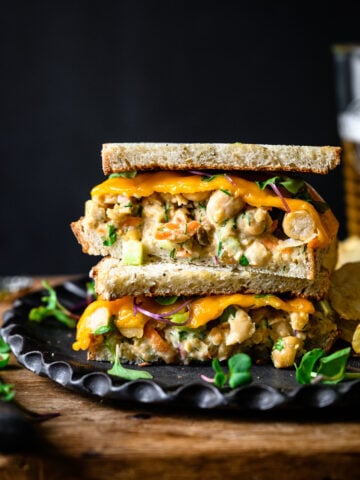 side view of a vegan tuna salad sandwich sliced in half and stacked on a plate with potato chips.