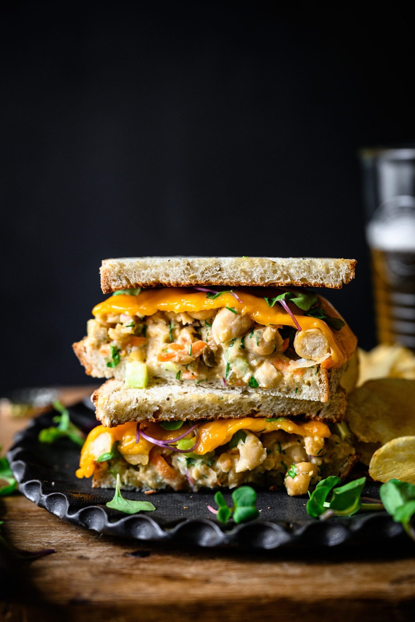 side view of a vegan tuna salad sandwich sliced in half and stacked on a plate with potato chips. 