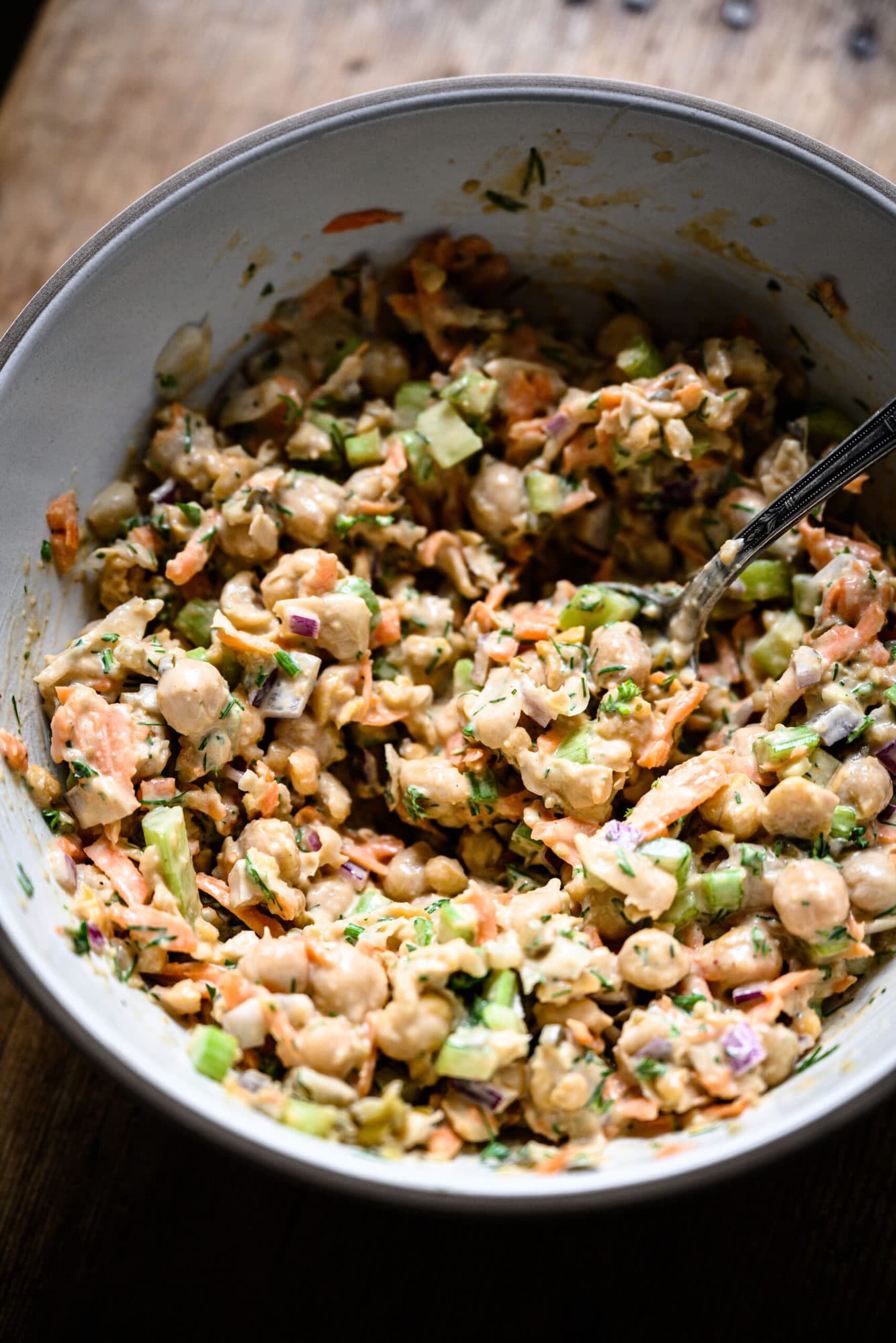 close up view of vegan chickpea tuna salad in a white mixing bowl with spoon.