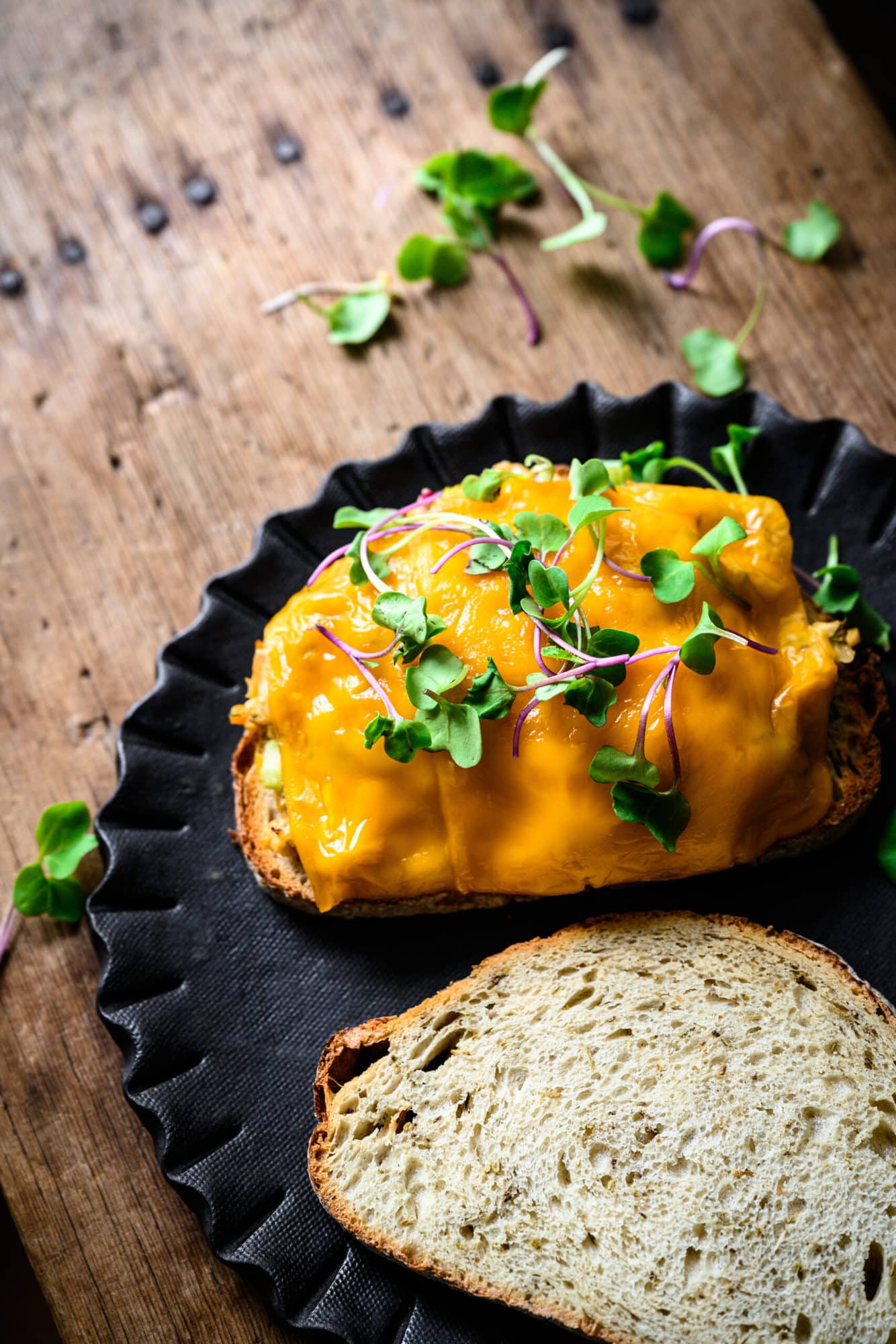 close up view of open face vegan tuna melt with melted cheese and microgreens on top.