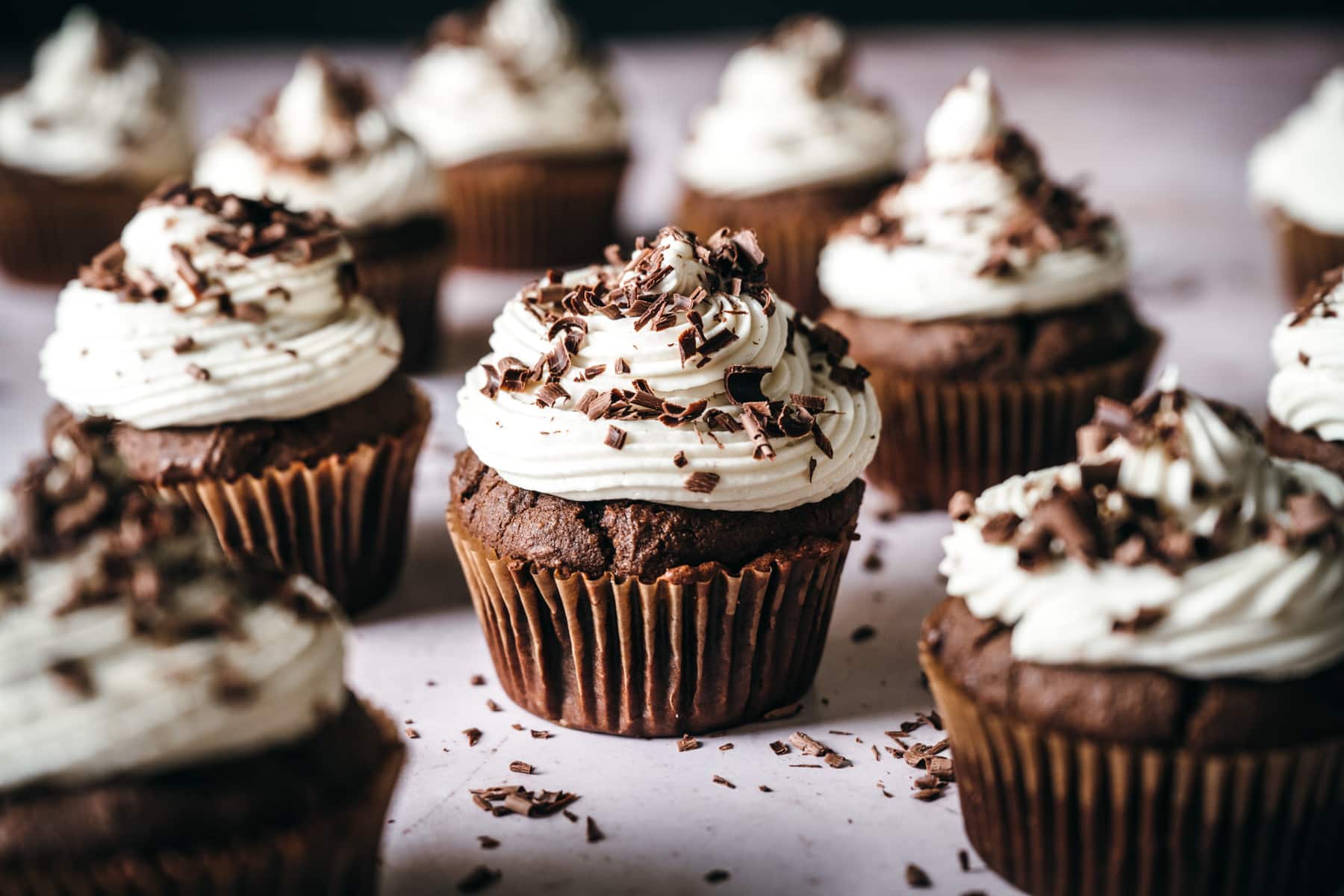 close up side view of vegan chocolate cupcake topped with vanilla frosting and chocolate shavings. 