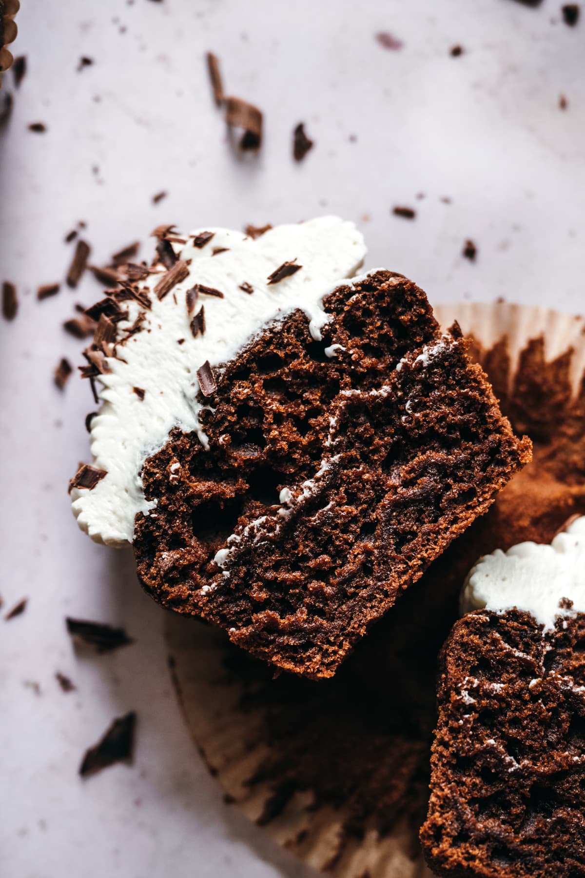 close up overhead view of vegan chocolate cupcake sliced in half with vanilla frosting. 