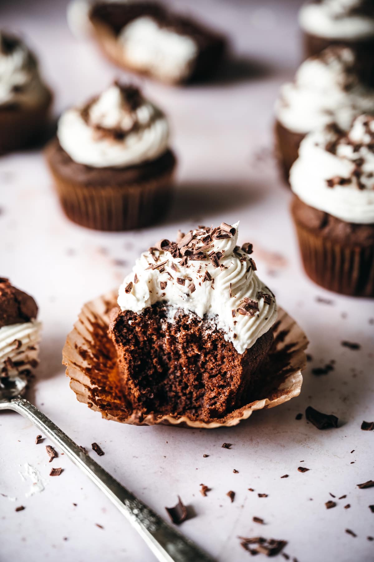 side view of vegan chocolate cupcake topped with vanilla frosting with bite taken out. 