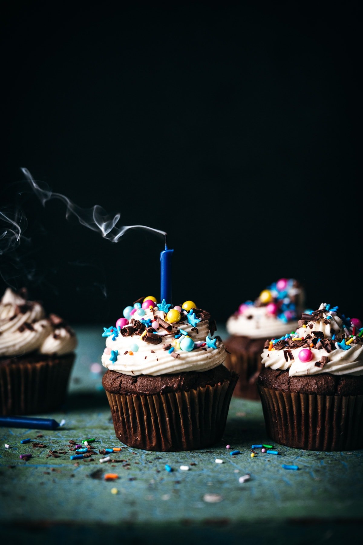 close up side view of vegan chocolate cupcakes with sprinkles and candle with smoke coming from top.