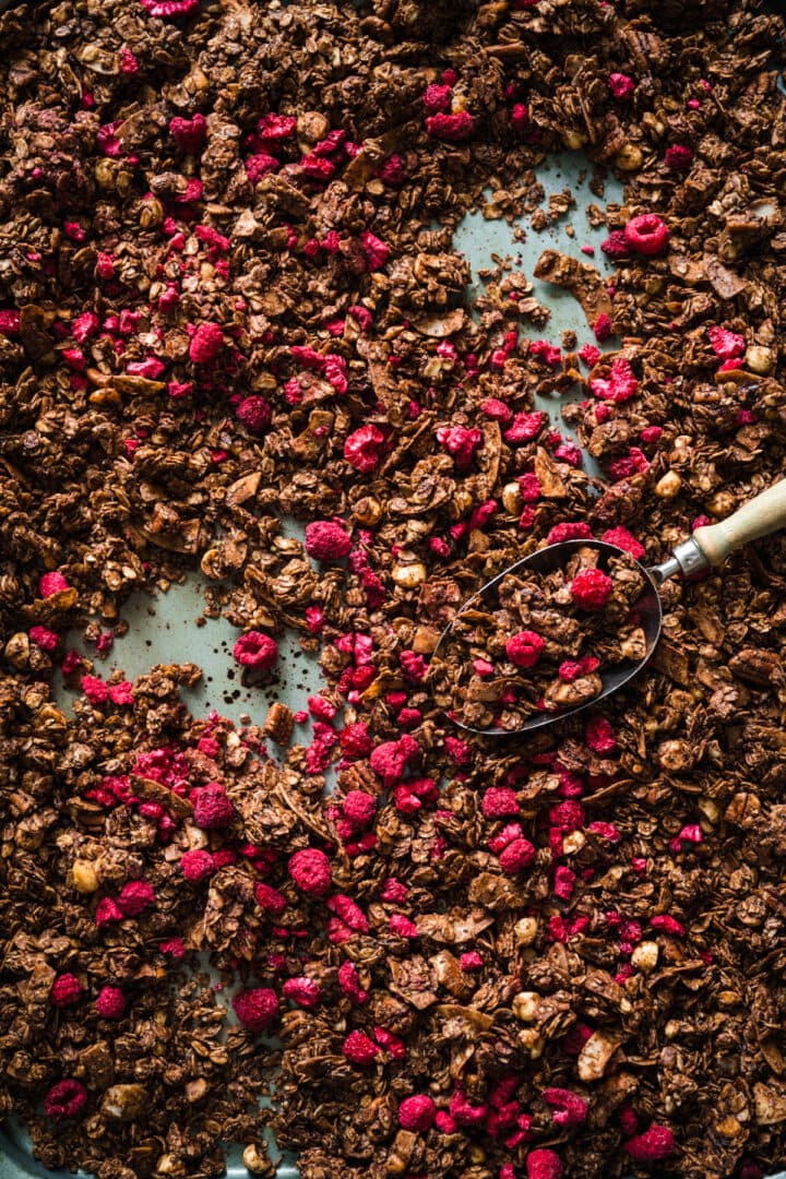 overhead view of chocolate hazelnut granola with freeze-dried raspberries on sheet pan.