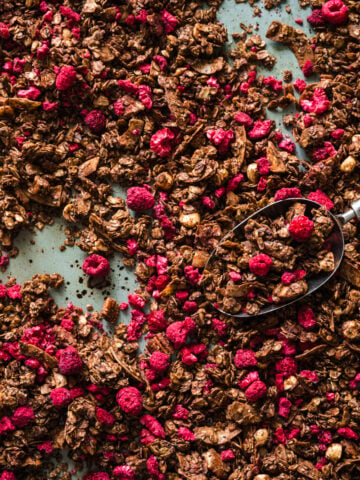 overhead view of chocolate hazelnut granola with freeze-dried raspberries on sheet pan.