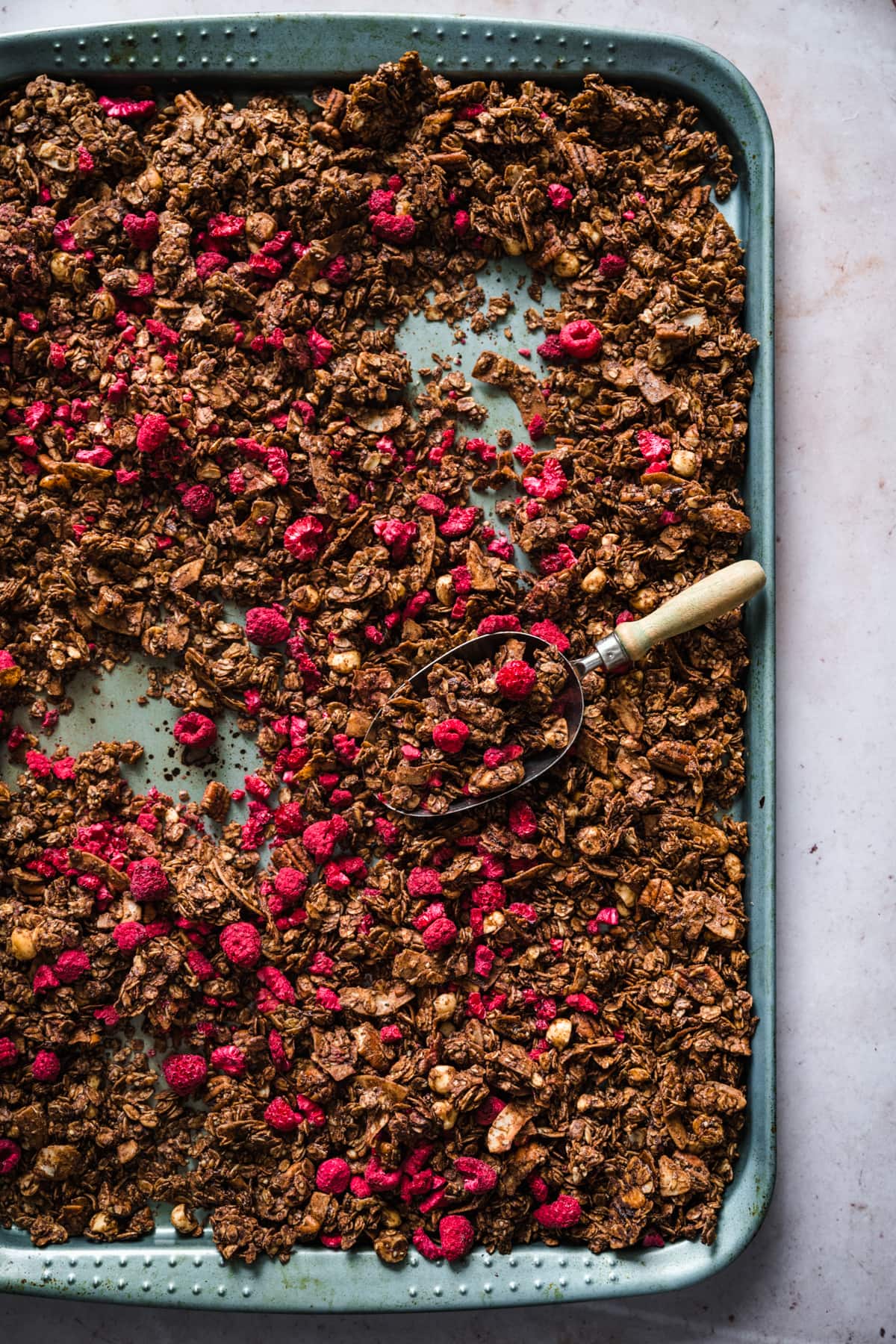 overhead view of chocolate hazelnut granola with freeze-dried raspberries on sheet pan.