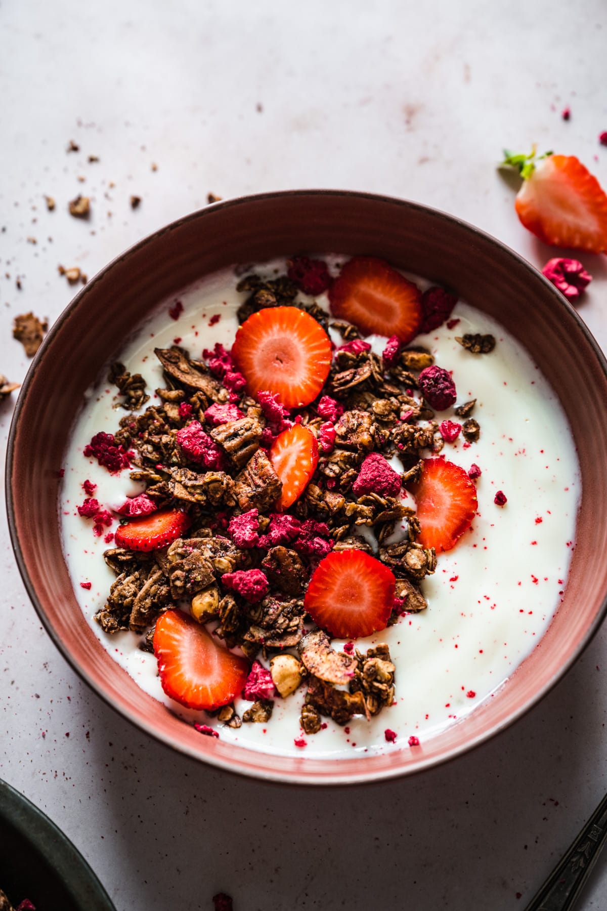 overhead view of chocolate hazelnut raspberry granola over yogurt with fresh strawberries.