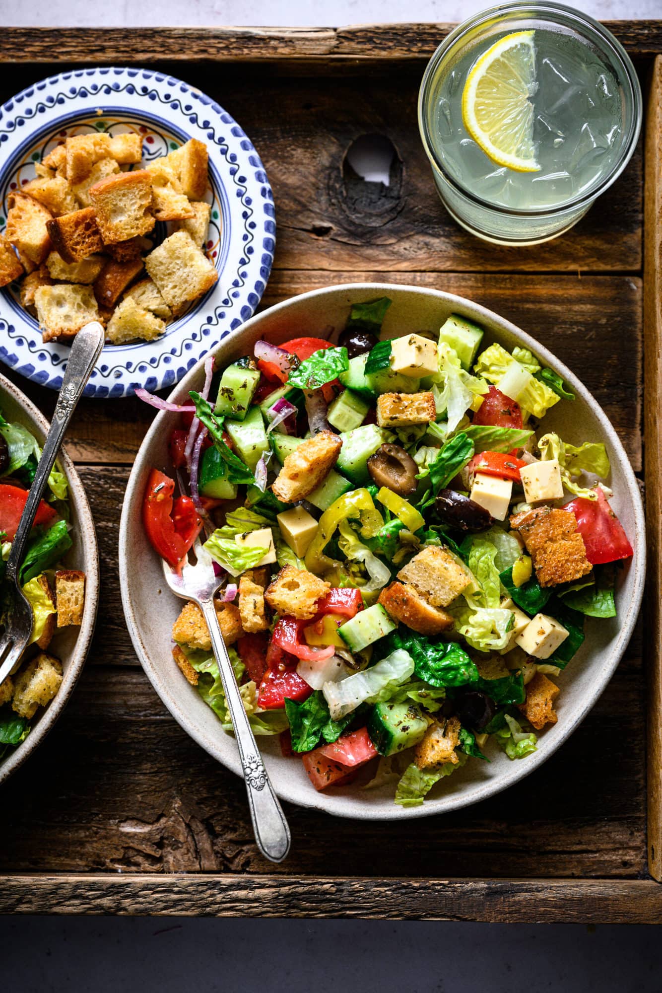 overhead view of vegan italian chopped salad in bowls on wood platter. 