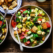 overhead view of vegan italian chopped salad in bowls on wood platter.