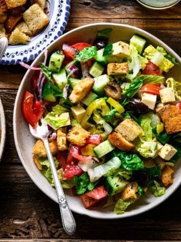 overhead view of vegan italian chopped salad in bowls on wood platter.