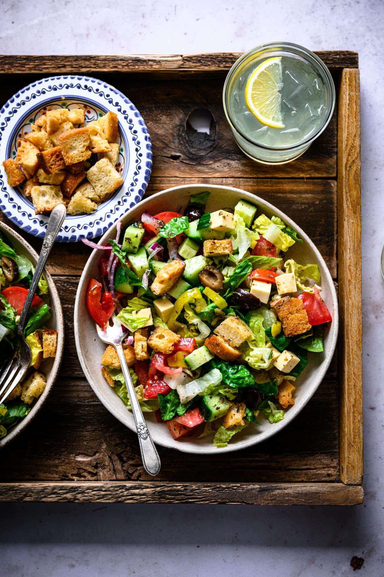 overhead view of vegan italian chopped salad in bowls on wood platter. 