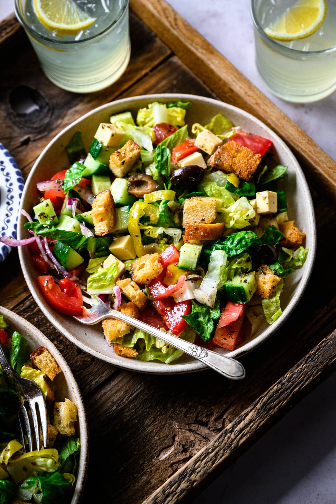 overhead view of vegan italian chopped salad in bowls on wood platter. 