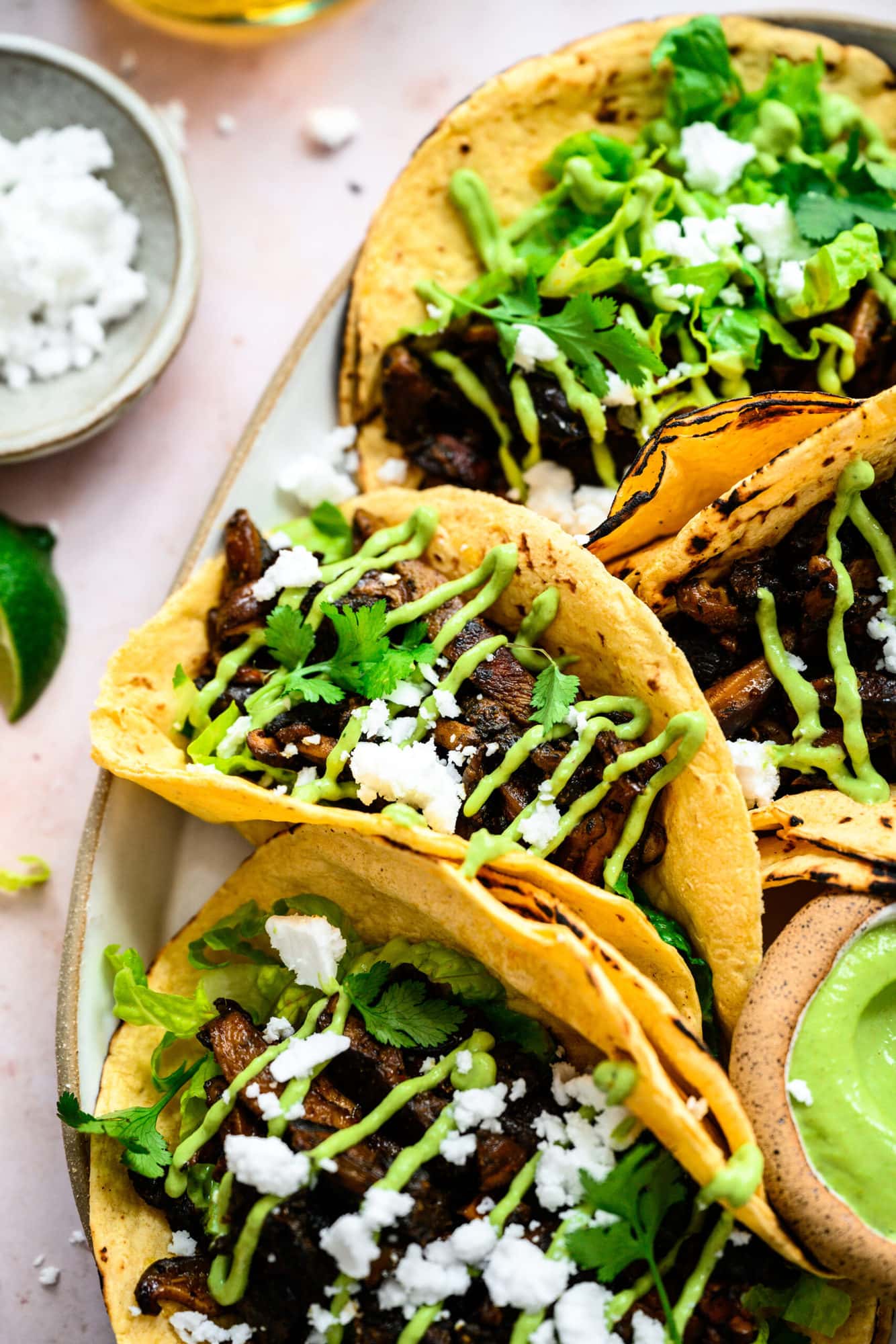 close up view of mushroom shawarma tacos on a platter with cilantro tahini sauce and feta. 