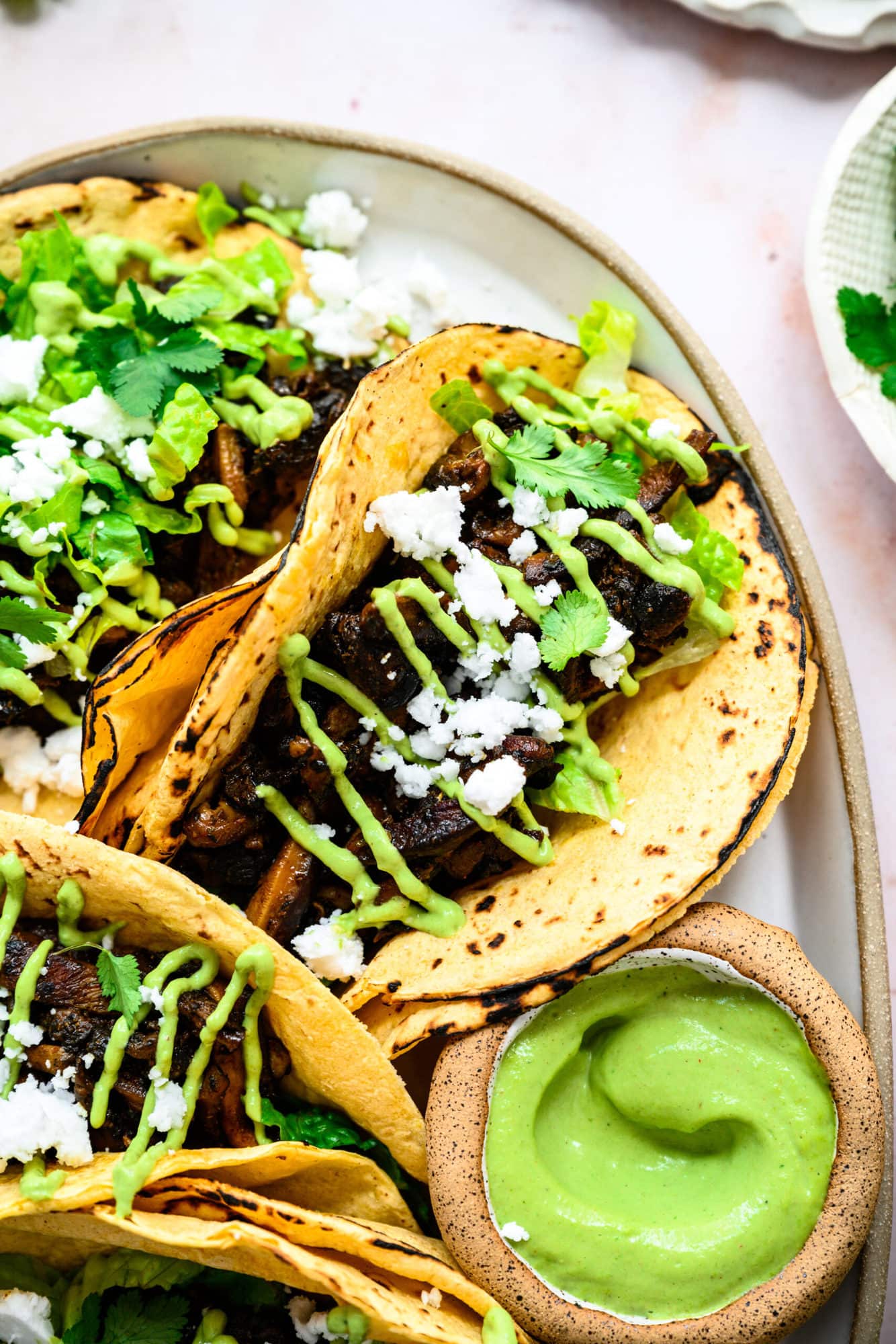 close up view of mushroom shawarma tacos on a platter with cilantro tahini sauce and feta. 