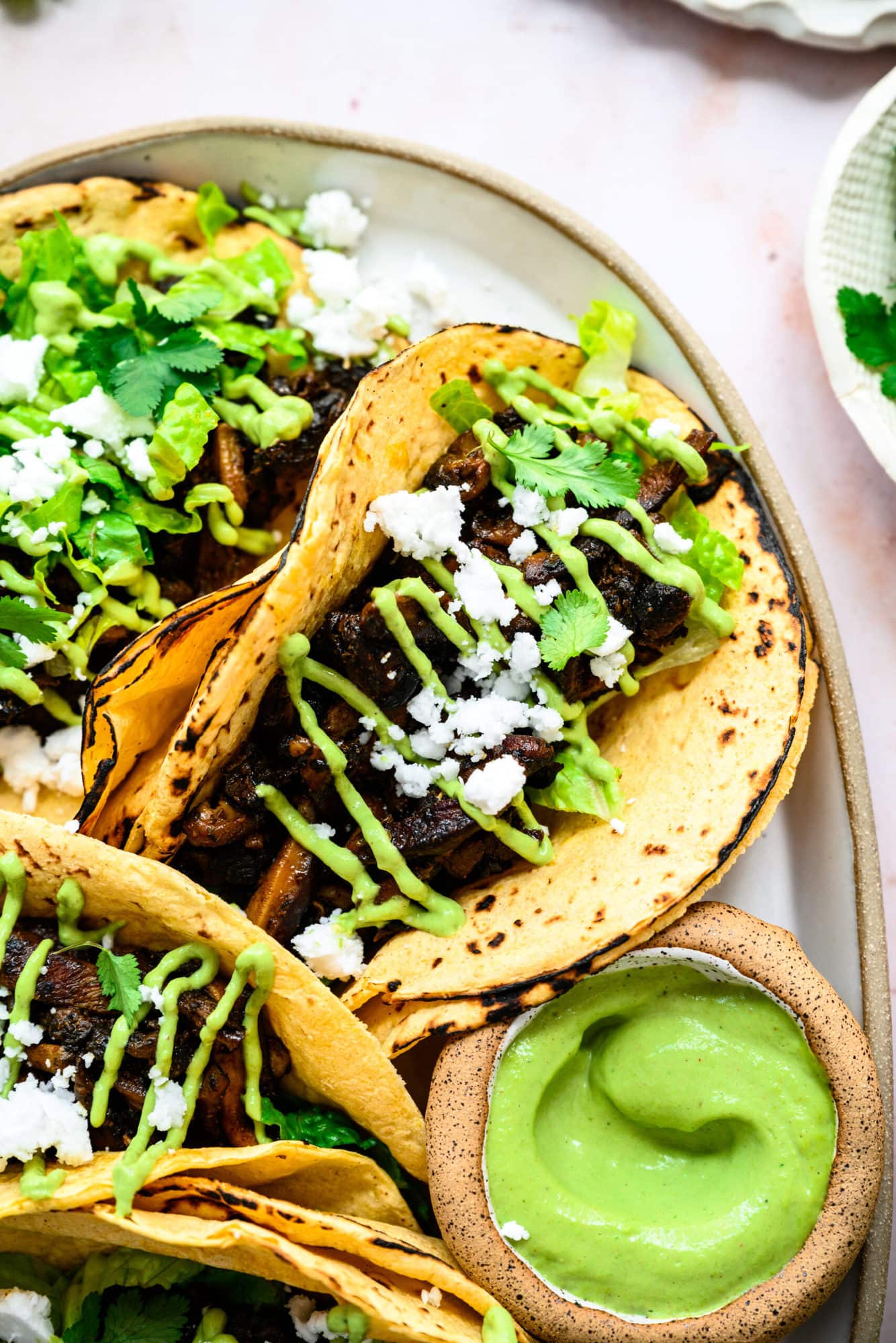 close up view of mushroom shawarma tacos on a platter with cilantro tahini sauce and feta. 