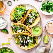 overhead view of mushroom shawarma tacos on a platter with cilantro tahini sauce and feta.