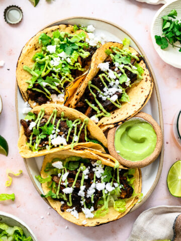 overhead view of mushroom shawarma tacos on a platter with cilantro tahini sauce and feta.