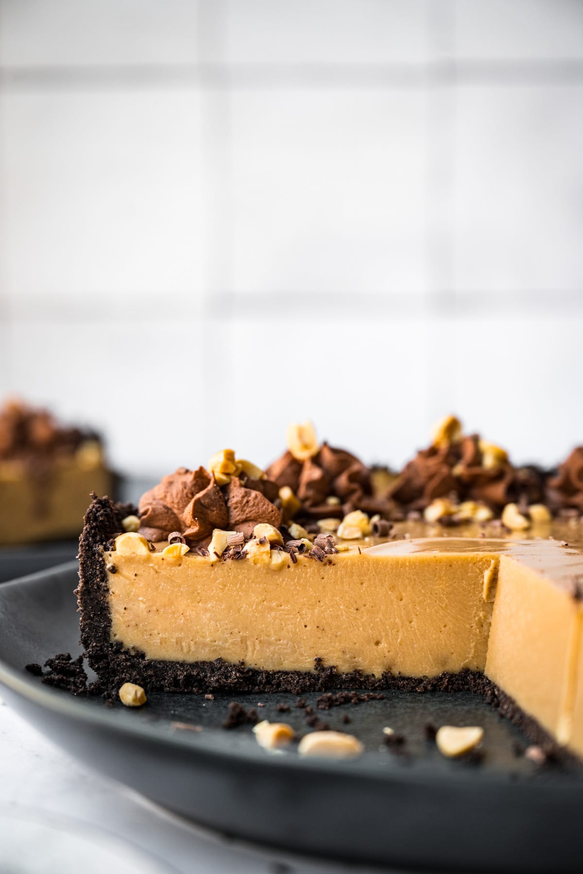 close up view of cross section of peanut butter pie with chocolate cookie crust on black plate. 