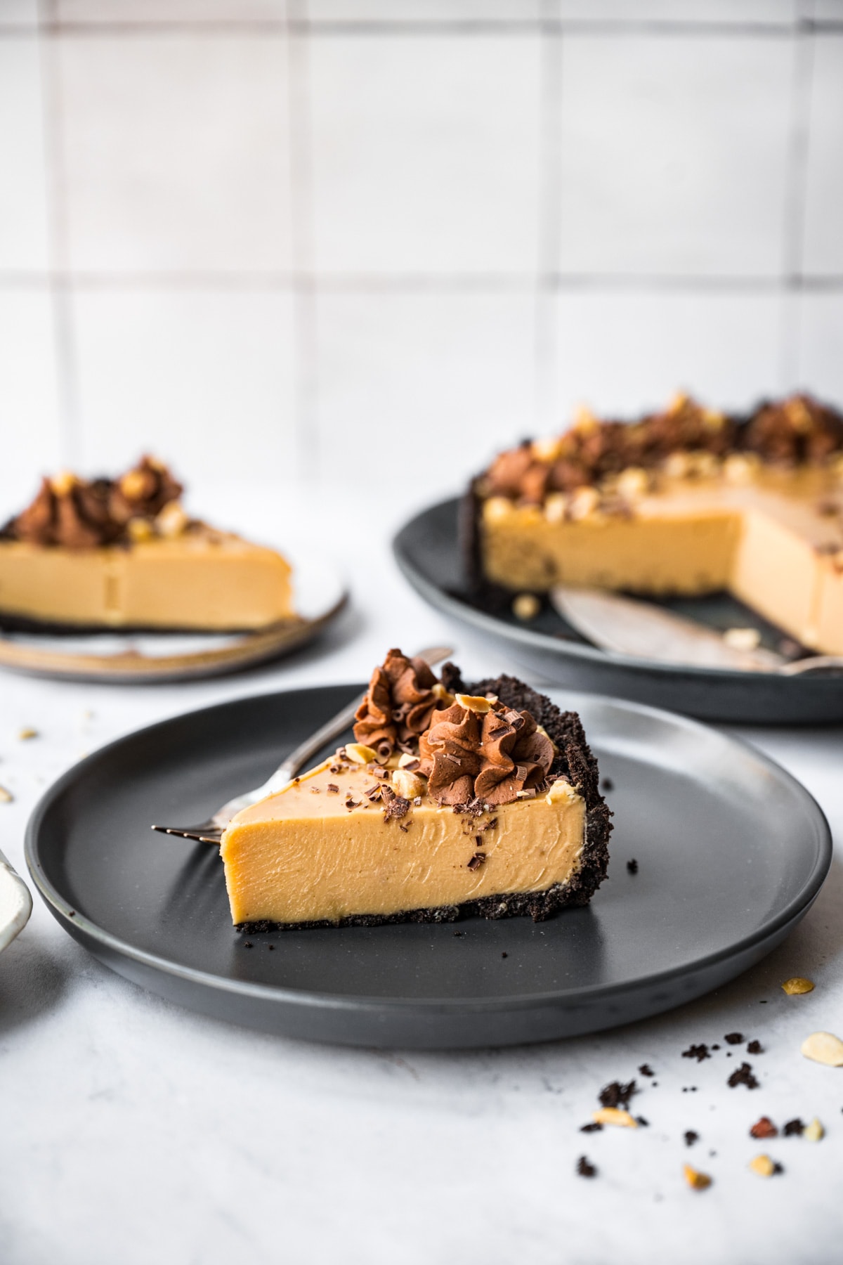 side view of peanut butter pie with chocolate cookie crust on black plate with fork. 