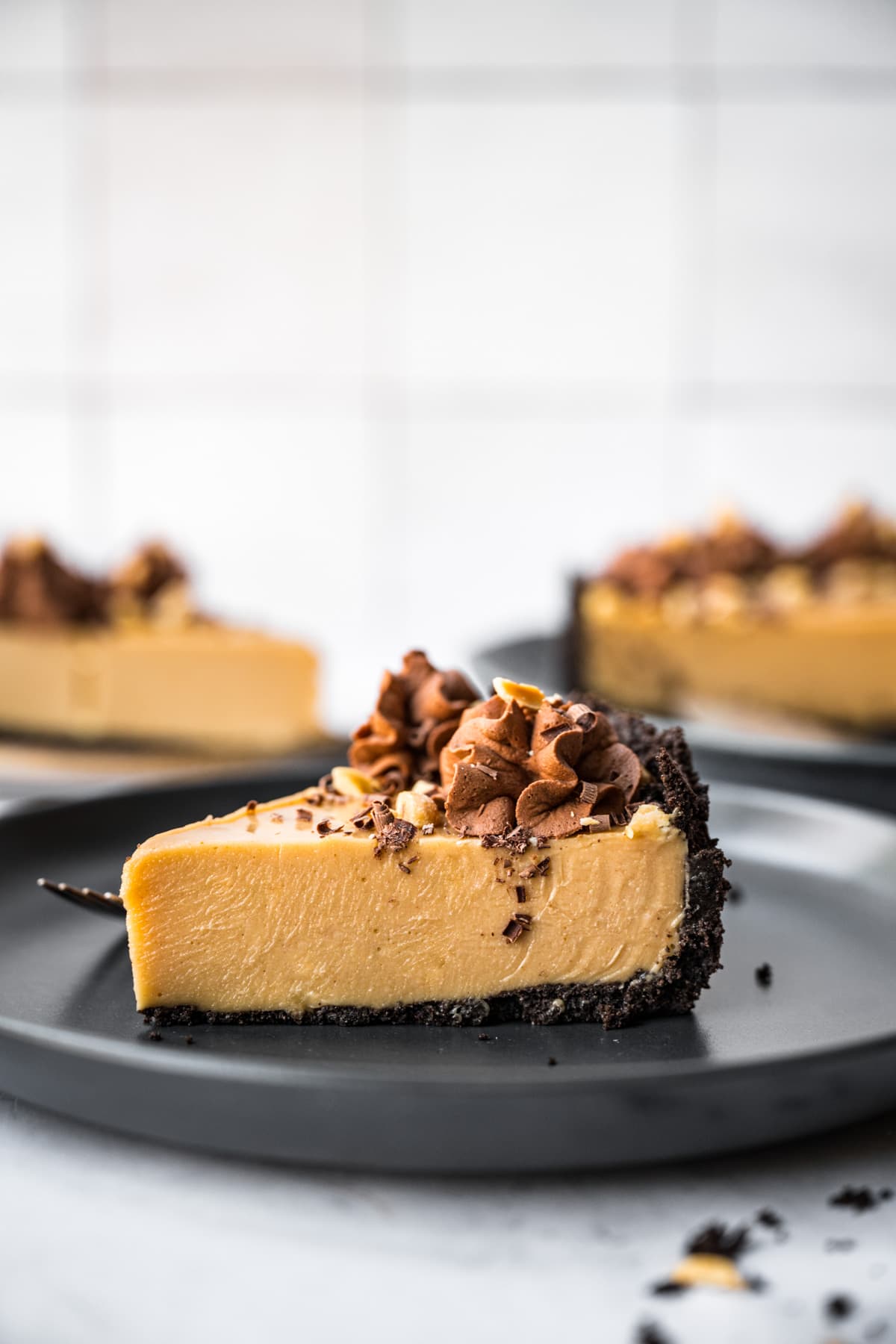 close up view of peanut butter pie with chocolate cookie crust on black plate. 